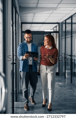 Two professionals discussing work while walking in an office hallway, fostering collaboration and teamwork.