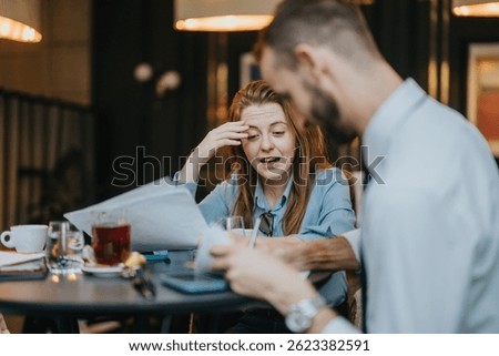 Two professionals are engaged in an animated conversation while working together in a cozy cafe environment, sharing ideas and analyzing papers to collaborate on their project.