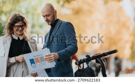 Two professionals examine charts and documents outdoors in autumn, standing beside a scooter. Warm colors and relaxed mood convey collaboration, planning, and a friendly professional connection.