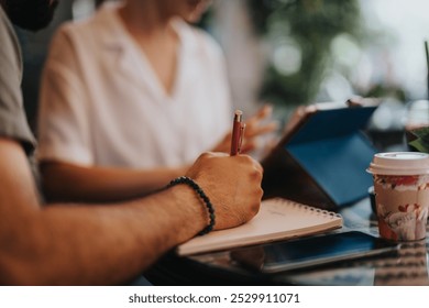 Two professionals having a business meeting in a coffee shop, taking notes and using a tablet. - Powered by Shutterstock