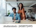 Two professionals, a man and a woman, collaborating in a modern office. They smile, looking at the camera. A creative workspace represents teamwork, diversity, and success.