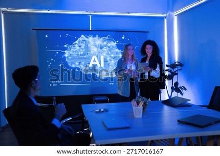 Two professionals present information about artificial intelligence in a bright office. A projector displays a cloud graphic, while a colleague analyzes data from a distance.