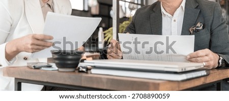 Two Professionals Reviewing Printed Documents Together At Table With Laptop And Office Supplies