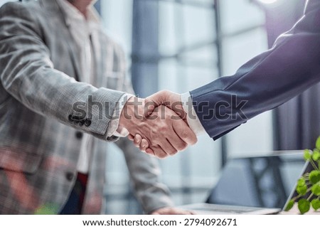 Two professionals shake hands in a bright, modern office. Their confident grip suggests mutual trust and agreement. The blurred background hints at a corporate or collaborative setting
