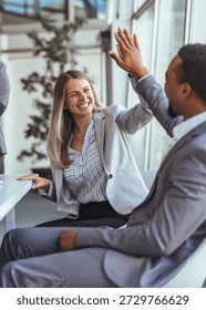 Two professionals share a high-five in a bright office, highlighting teamwork, celebration, and positive energy in a modern business environment.