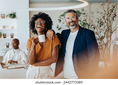 Two professionals stand in an office, holding coffee cups. They are happy and smiling, reflecting teamwork and success. Business man and business woman showing professionalism and confidence. - Powered by Shutterstock