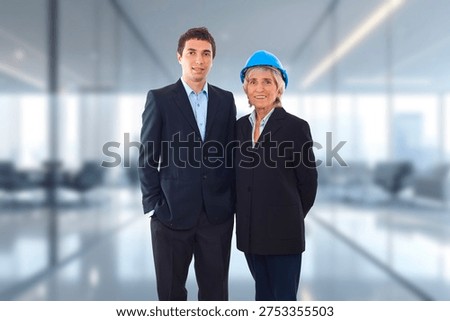 Two professionals stand side by side in a modern office space. One wears a blue hard hat, suggesting construction or engineering roles. The other, in a suit, conveys formal business presence