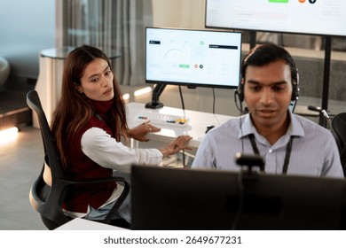 A two professionals are working modern tech customer support office. man wearing headset is focused his computer screen, while woman looks another monitor displaying analytics. environment