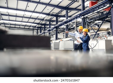 Two project managers standing in modern industrial factory. Manufacturing facility with robotics, robotic arms and automation. Storing products and materials in warehouse.