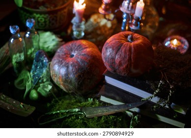 Two pumpkins rest on a stack of books beside candles and small glass bottles. table is decorated with green moss and various objects that hint at a mysterious theme.