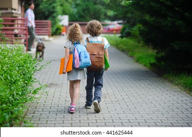 Zwei Schüler der Grundschule gehen Hand in Hand. Junge und Mädchen mit Schultaschen hinter dem Rücken. Beginn des Schulunterrichts. Warmer Herbsttag. Zurück zur Schule.  Kleine erste Grader.
