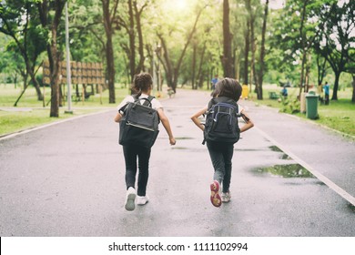 Two Pupils Of Primary School Run Go To Shool. Two Girl With Bags Behind The Back. Warm Day Of Fall. Back To School. Little First Graders.
