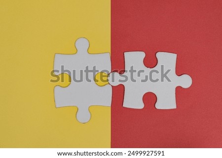 Two puzzle pieces are interlocking on coloured background. It’s fitting in, completing tasks, or finding solutions to problems concept