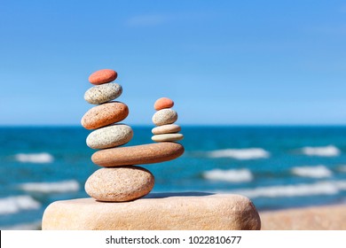 Two pyramids of colored balanced rocks on a background of blue sky and summer sea. Concept of balance, harmony and meditation