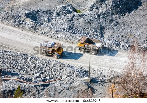 Two\
quarry dump trucks at the bottom of a stone\
pit