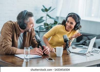 two radio hosts in headphones laughing while recording podcast in studio together - Shutterstock ID 1433456504