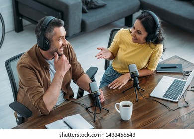 Two Radio Hosts Talking And Smiling While Sitting Near Microphones In Broadcasting Studio