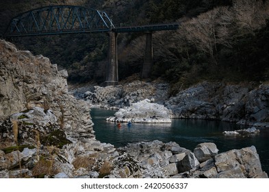 Two rafter cruising with canoe under a railway bridge on Yoshino river on January 2024 in OBOKE Canyon, Shikoku, Japan. Yoshino River is one of the most popular among rafters in Japan.