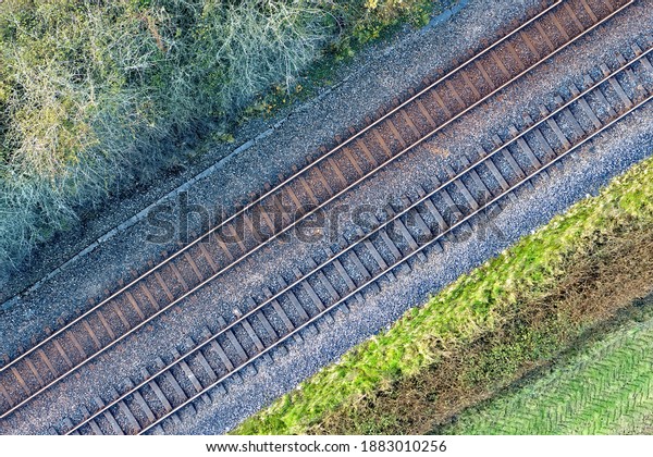 Two railway tracks which consists of two parallel\
steel rails, anchored perpendicular to members called ties\
(sleepers) of concrete to maintain a consistent distance apart, or\
rail gauge. With trees.