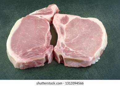 Two Raw Center Cut Bone In Pork Chops On Black Cutting Board