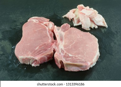 Two Raw Center Cut Bone In Pork Chops With Excess Fat Trimmed Off On Black Cutting Board For Healthy Lower Cholesterol Meal