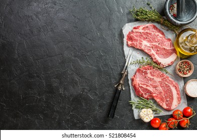 Two raw fresh marbled meat black angus steak ribeye and seasonings on black stone background. Top view - Shutterstock ID 521808454