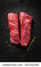 Two raw hanger steaks, also known as butchers steak or hanging tenderloin with rosemary, pepper and salt on dark background