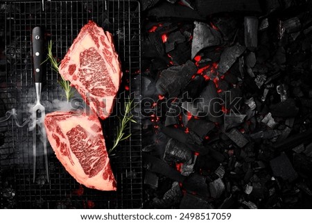 Two raw marble ribeye steaks are prepared over hot coals. On a black charcoal background. Top view.