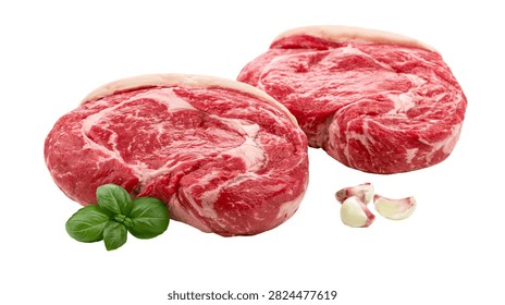 Two raw marbled ribeye beef steaks with fresh green basil leaves and garlic cloves