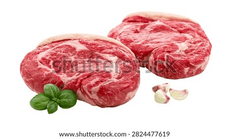 Two raw marbled ribeye beef steaks with fresh green basil leaves and garlic cloves