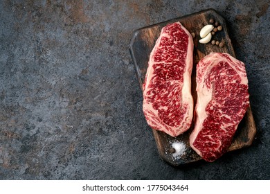 Two raw new York steaks on a chopping Board with seasonings and garlic. Wagyu meat for grilling, top view and copy space
