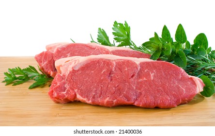 Two Raw Porterhouse Steaks On A Wooden Chopping Board With Herbs