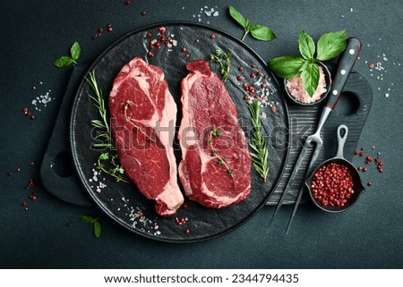 Two raw rib eye beef steaks with spices on a plate. Ready to cook. On a dark stone background. Top view.
