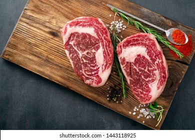 Two raw rib eye steak on the butcher's Board on a wooden table prepared prepared for cooking. Marbled beef top view
