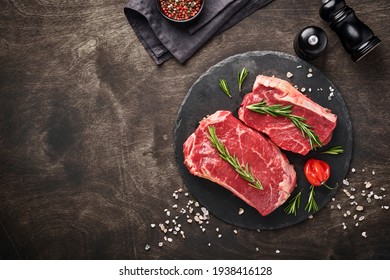 Two raw steak New York  with rosemary and spices on a piece of parchment paper on old dark stone background. Top view. Mock up. - Powered by Shutterstock