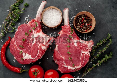 

two raw steaks, beef tomahawk with spices and thyme on a stone background.