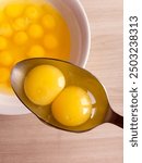 Two raw yolks of quail eggs in a spoon. Broken eggs. The benefits or harm of yolks. Cooking dishes from eggs.