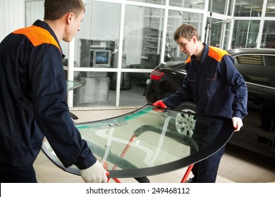 Two Real Mechanics Changing The Broken Windshield Of Black Car In Auto Repair Shop