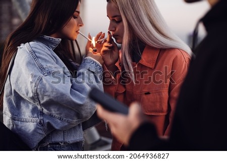 Two rebellious teenage girls are standing outdoors and lighting cigarettes. Teenagers smoking.