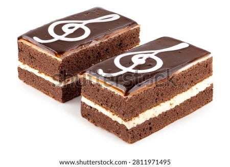 Two rectangular chocolate sponge cake slices with white cream layer and treble clef icing design, isolated on a white background.