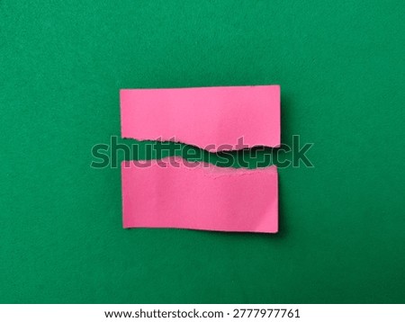 Two rectangular pieces of pink paper with rough, torn edges are placed parallel on a solid green background.