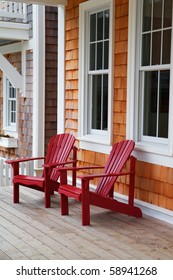 Two red Adirondack chairs on a wood deck against a brown wood shake home
