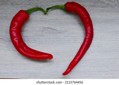 Two Red Bitter Peppers Lie In The Shape Of A Heart. The Figure Of A Pepper Heart. Gray Background, Space For Text. Vegetables, Spicy, Bitter,. High Quality Photo