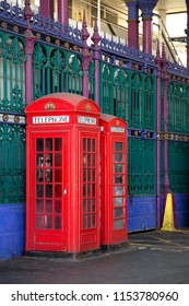 Two red booths in two different sizes with green and blue iron fence in background in Smithfield market in London UK