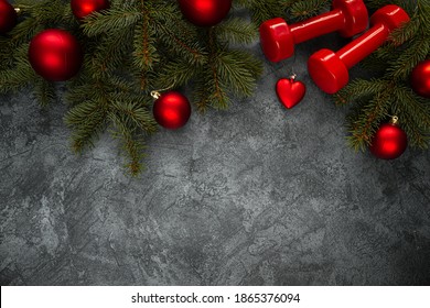 Two red dumbbells, Christmas tree branches with decorations, ornaments and baubles. Healthy fitness lifestyle holiday season composition. Flat lay with copyspace on dark background.
