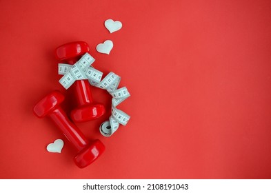 Two red dumbbells, white measuring tape hearts on red background with copy space. Concept of Valentines day, healthy lifestyle, giving gifts, love of sports, shopping