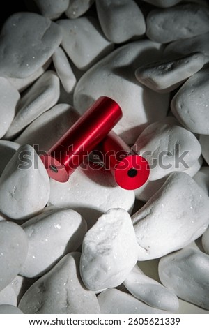 Two red dummy cartridges for dry firing, lying on smooth white stones, creating a striking contrast between vibrant red and neutral white, ideal for firearm training and safety visuals.