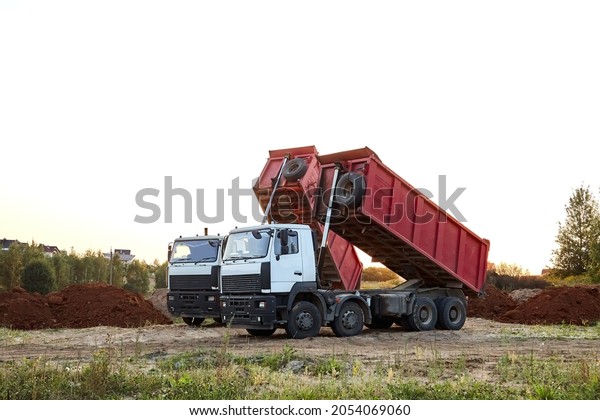 Two red dump trucks simultaneously lifted the\
bodies to unload the sand. Cargo transportation services. Large\
multi-ton truck. Unloading cargo. Construction site and machinery.\
Banner. Common view.
