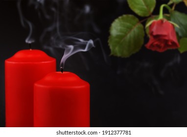 Two red extinguished candles with white smoke and withered rose flower on black background