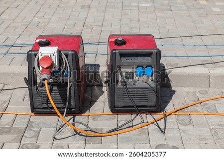 Two red generators are plugged into a power source. One of the generators is on the left and the other is on the right